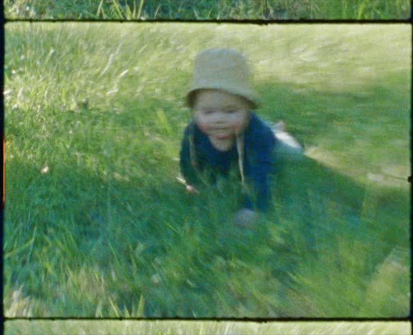 A baby boy with a hat crawling on grass