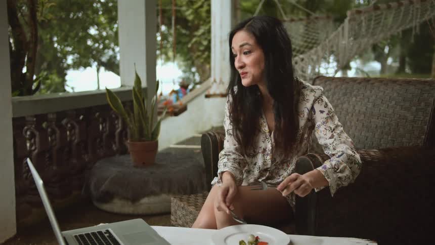 A woman eats outside while interacting with her laptop