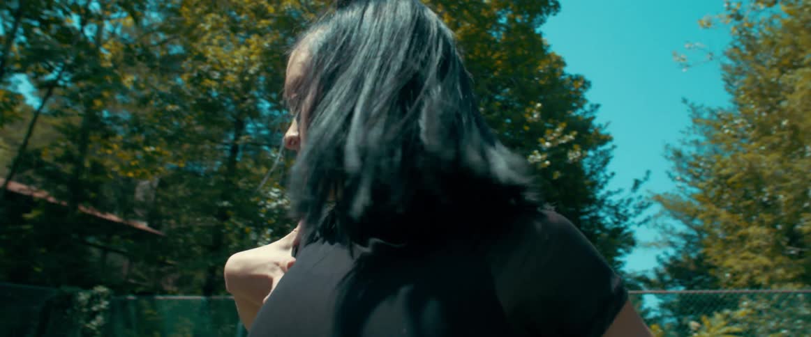 Woman with black hair dances near the chain link fence