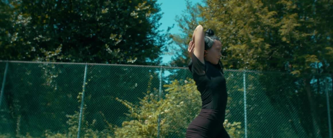 Girl dances outdoors on sports court enclosed by fence under blue sky
