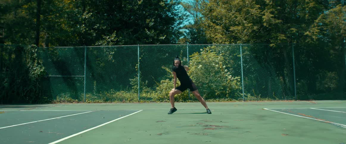 Young fit woman energetically dancing near the wire fence on a tennis court at daytime
