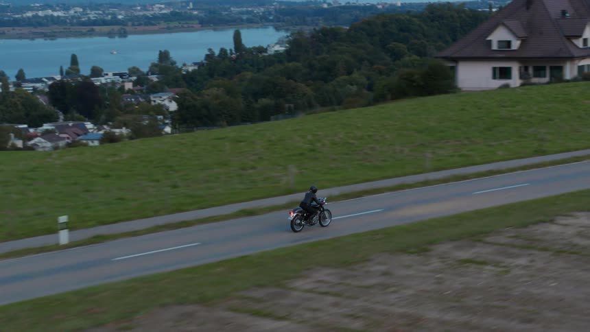 Person riding a motorcycle on a road through a negihborhood at evening
