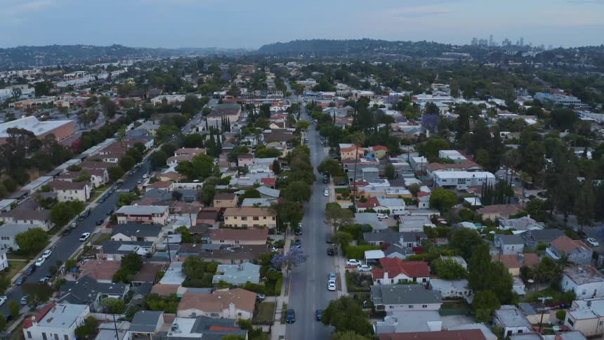 Traffic drive along street through neighborhoods while fog covers hills and city skyline on the horizon