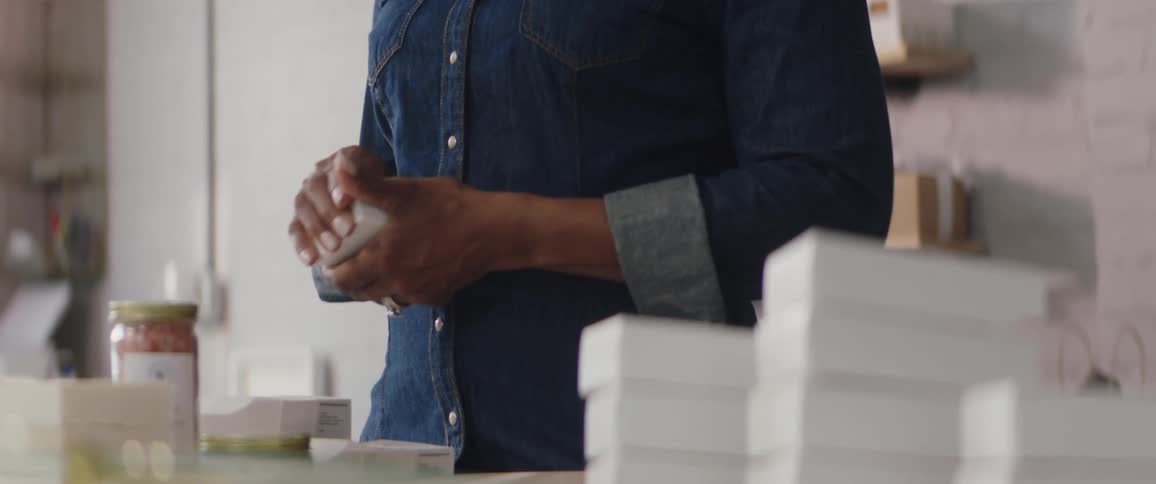 A woman in a room closing a box with shelves and a wall in the background