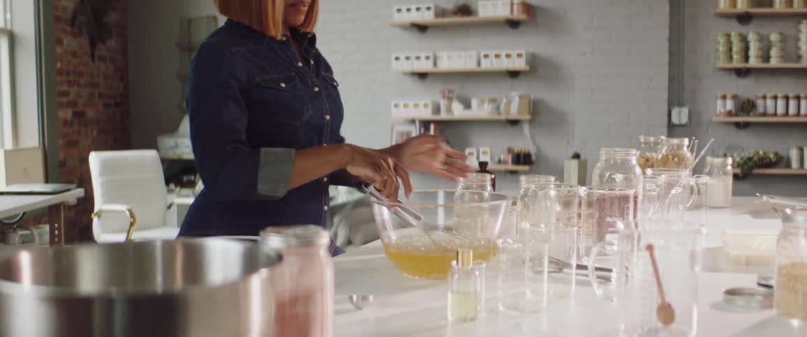 A woman in a room mixing a liquid in a bowl with a whisk with a wall and window in the background