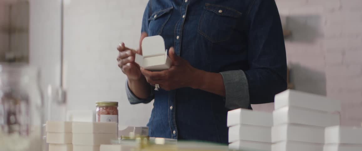 Woman stands over table full of soap and cartons boxing bars of soap