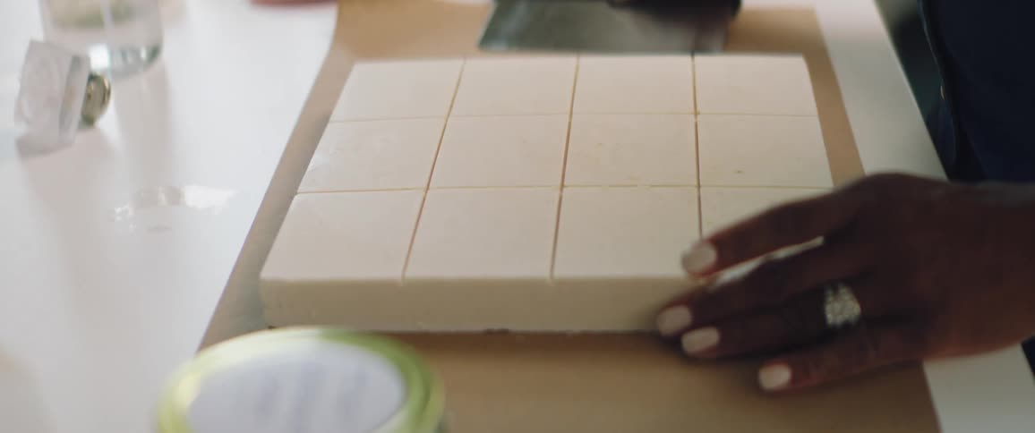 A woman straightens out a sheet of soap that has been partially cut into bars
