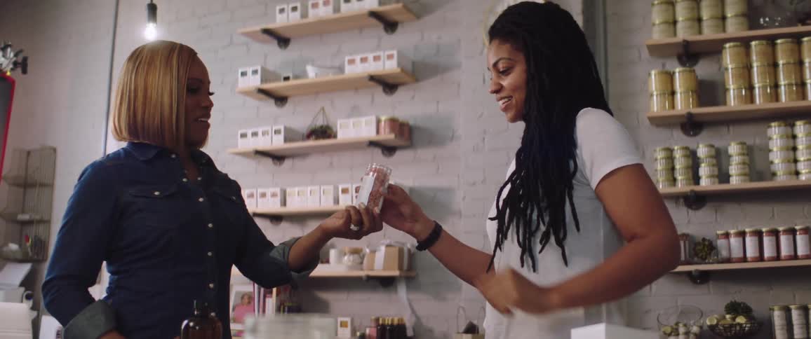 A saleswoman in a store opens a jar and hands it to a customer for her to smell
