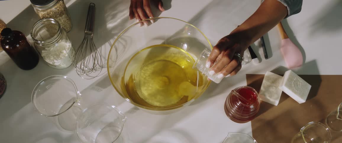 A woman pours an ingredient into a large glass bowl