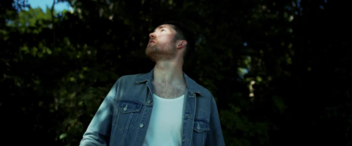 A man looks up at the trees as he walks through a forest