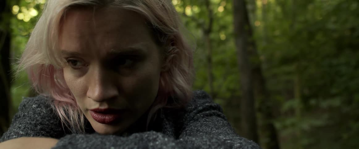 A woman is sitting in a forest and looks scared