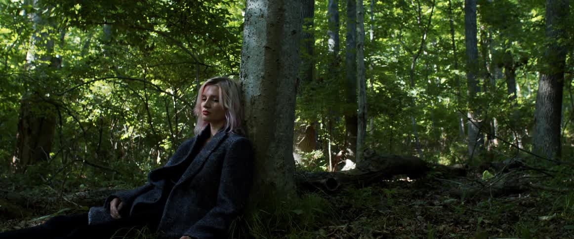 A woman sitting in a forest next to a tree
