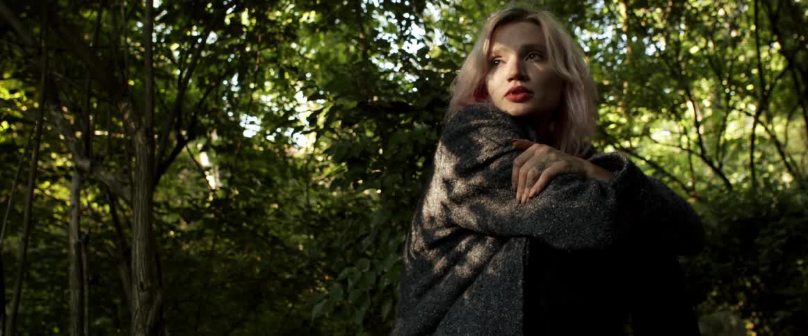 A woman sits hugging herself while looking at the trees on a sunny day