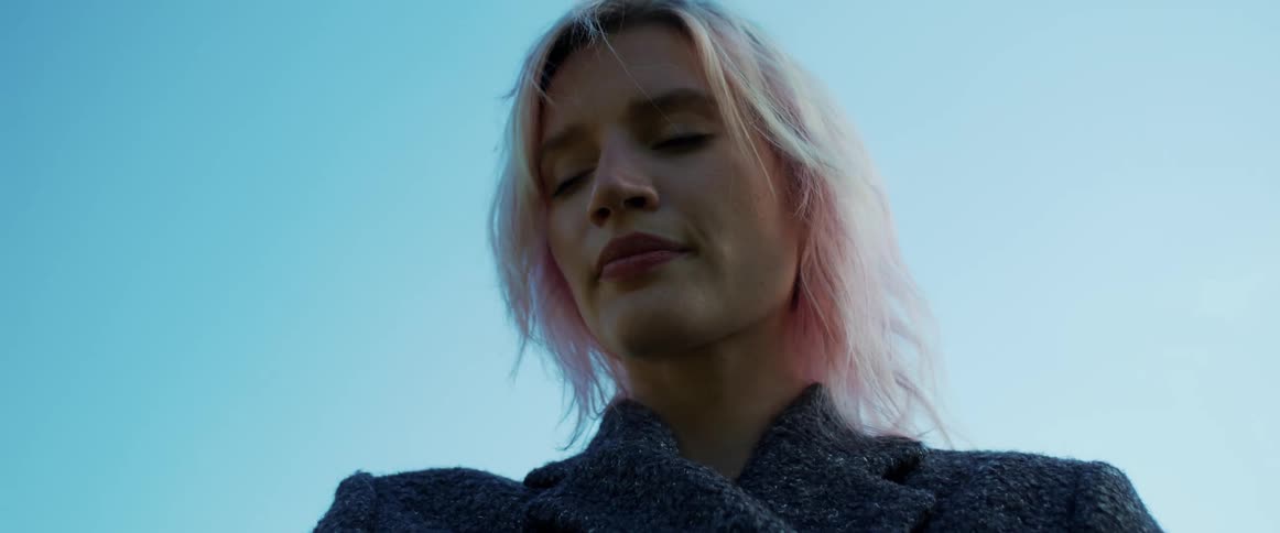 Blonde woman turns to look over her right shoulder while under a blue sky