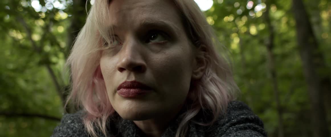 Blonde woman raises her head and looks sad while she is in the forest