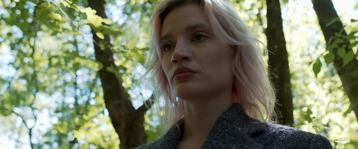 Blonde woman stands in a forest on a sunny day
