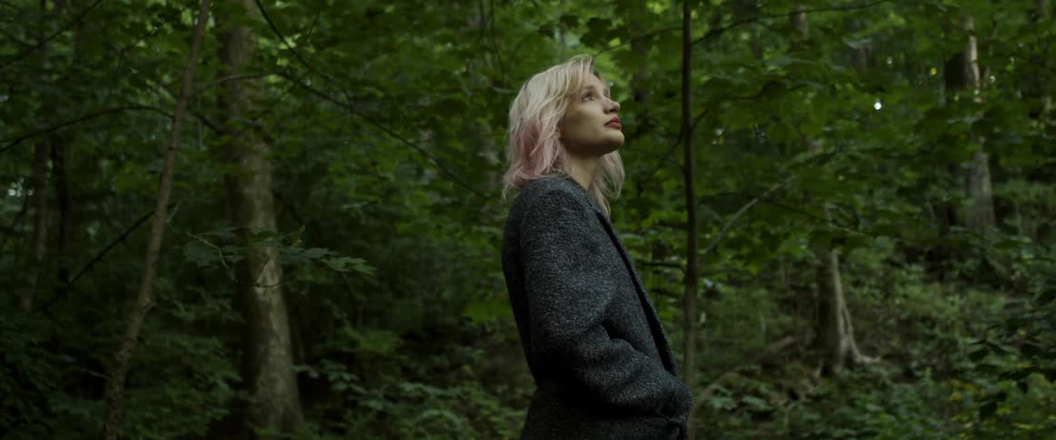 A woman in a dark jacket standing alone in a forest