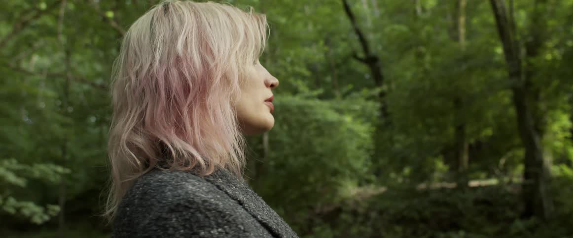 Blonde woman turns around while standing in the forest