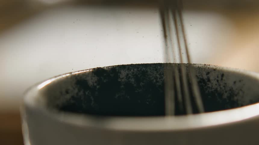 A whisk mixes a powdery substance in a white cup