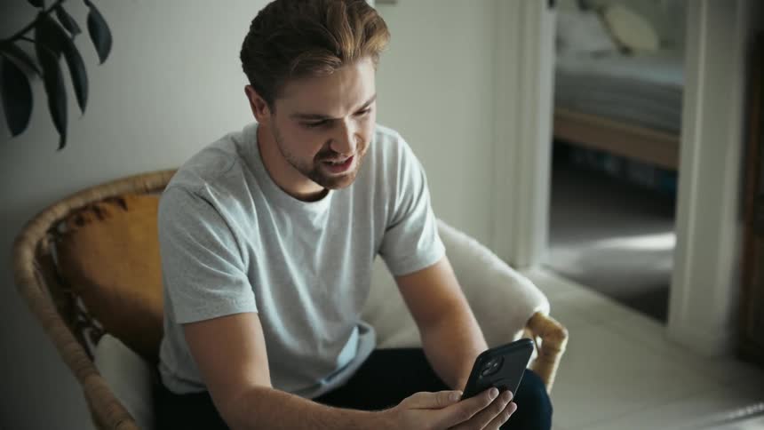 Young man laughing while talking on the phone while sitting at home