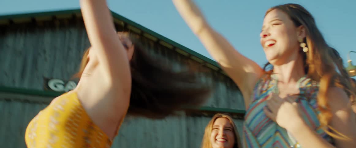 A pair of young women happily dance together while surrounded by many others at a party