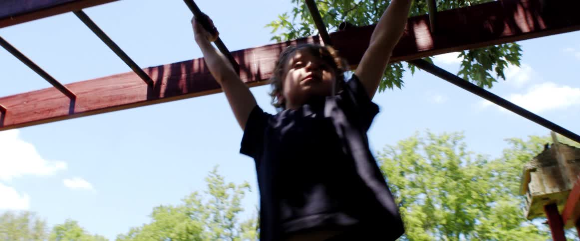 A boy playing on monkey bars with trees the sky and clouds in the background