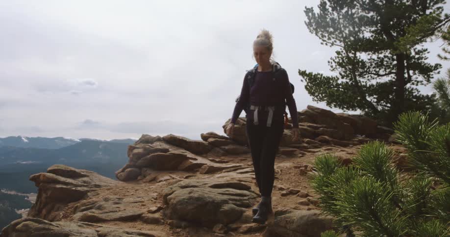 A woman hikes along the cliff of a mountain with a dog on a cloudy day