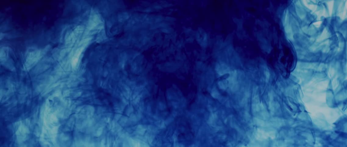 A blue liquid mixes with a clear liquid to create a darker cloudy suspension
