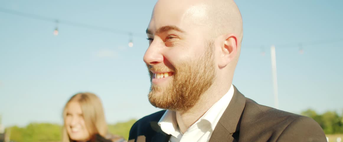 Man and woman smile as they stand outdoors under a blue sky