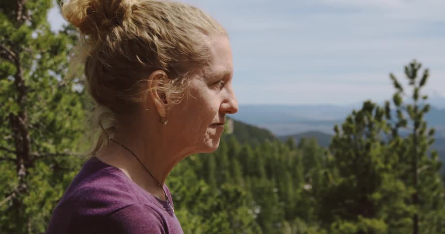 A woman standing in a forest looks across the landscape