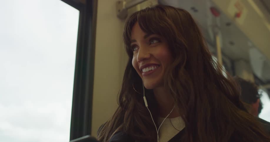 A woman smiles while looking out a window after sending a text on a smart phone