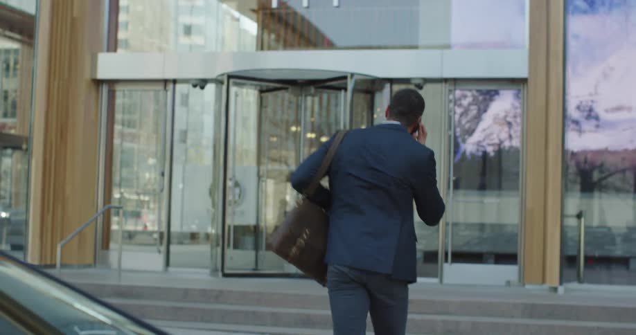 Black talks on his cell phone as he exits a vehicle and walks across the street and enters a building
