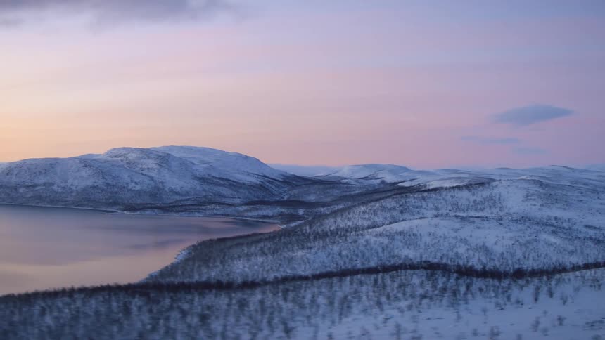 Snowy hills next to still lake against purple sky