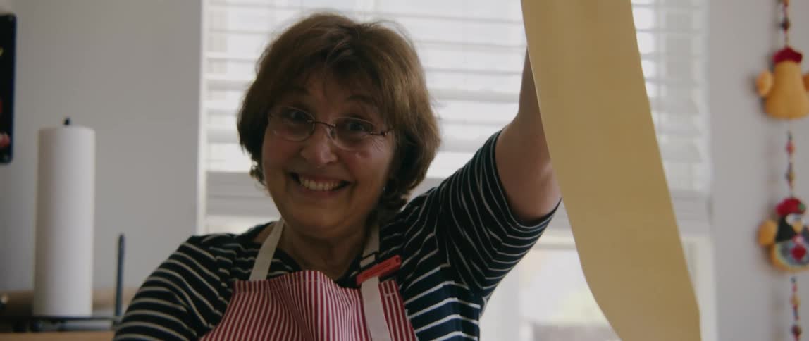 A woman in a kitchen kneading dough with a wall and a window in the background