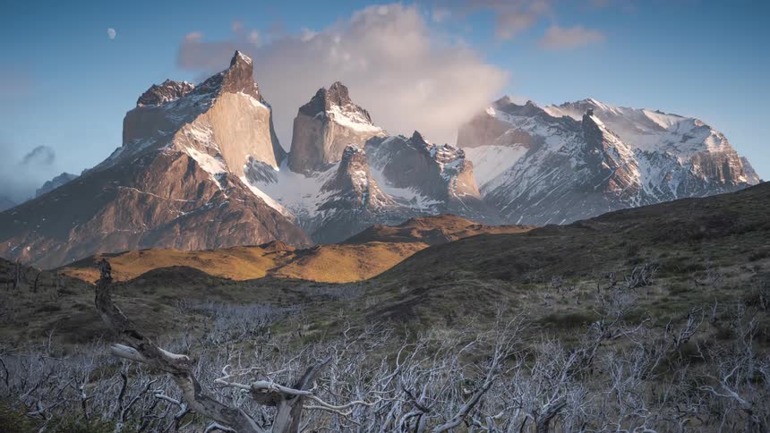 A landscape with a mountain range with snow and ice with the sky and clouds in the background