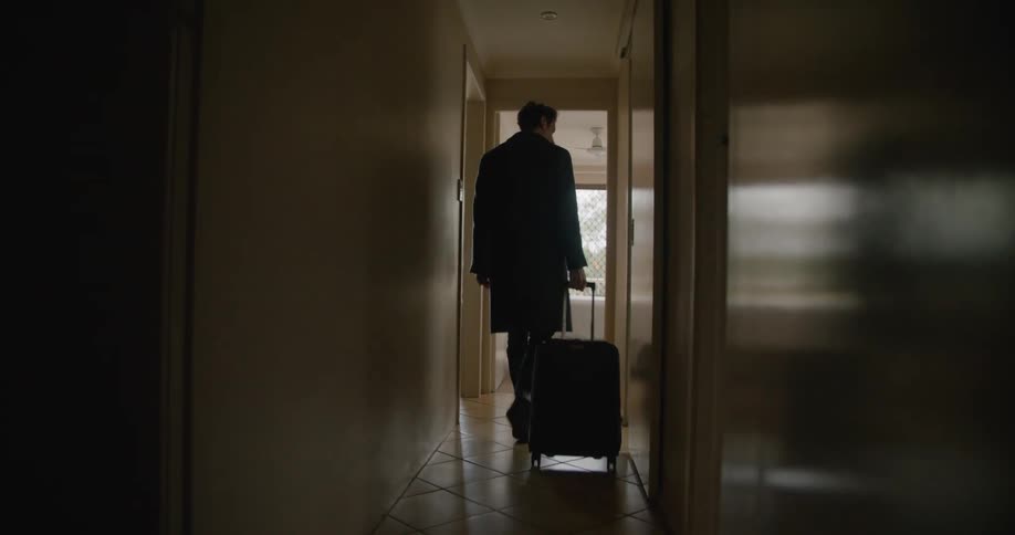 Man walks down narrow hallway pulling suitcase on wheels