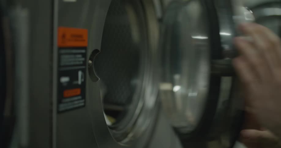 Person puts clothes in washing machine at laundromat