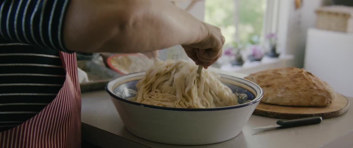Woman wearing an apron mixes pasta dish standing at kitchen counter