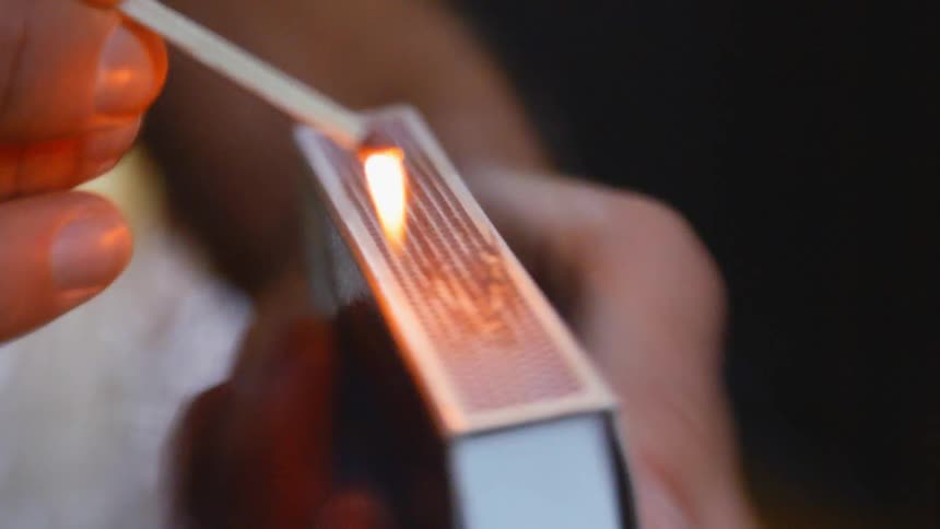 A person striking and lighting a match on the side of a matchbox