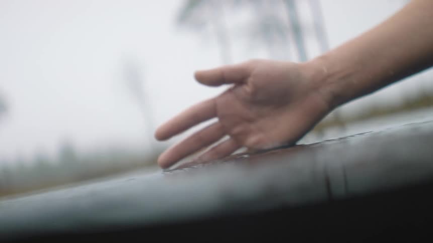 A person dipping their hands in water with trees the sky and clouds in the background