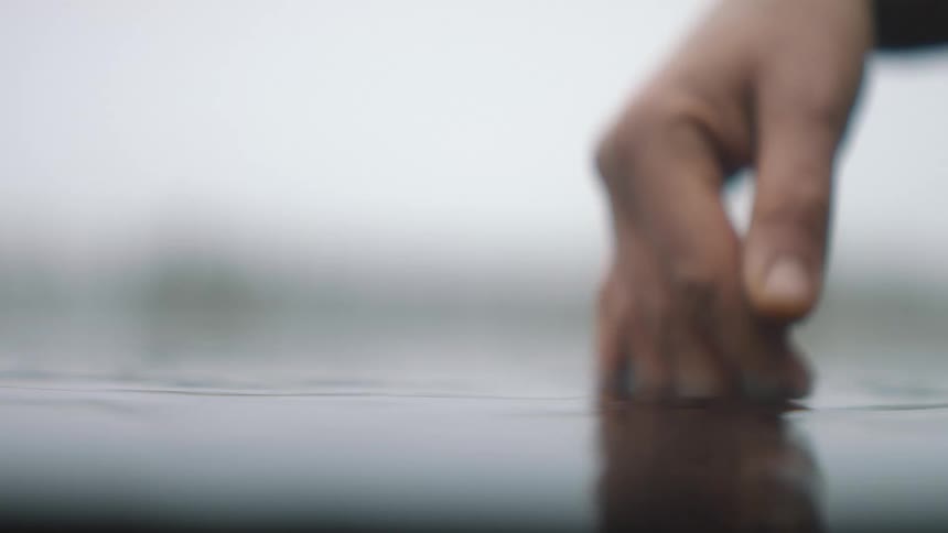 A person dipping their fingers in rippling lake water in nature