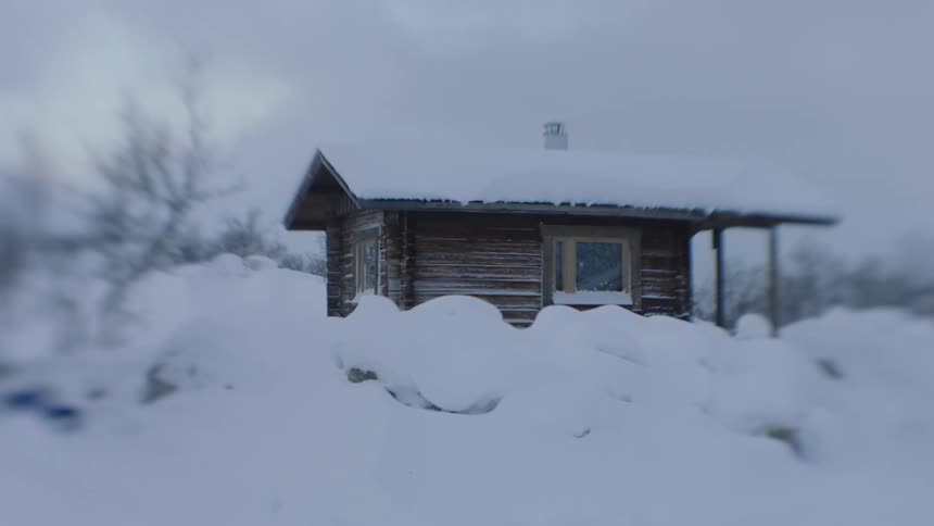 A small cabin surrounded by densely packed snow on a cloudy day