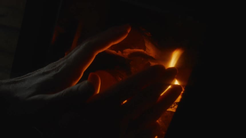 A pair of hands warming by a small fire under a pile of papers