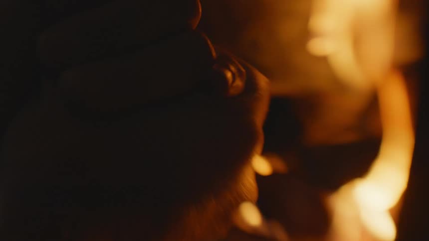 A person in a room rubbing their hands with a fireplace fire and smoke in the background
