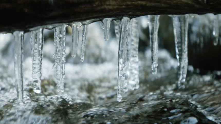 Several small icicles hang from a branch located over a flowing stream of water