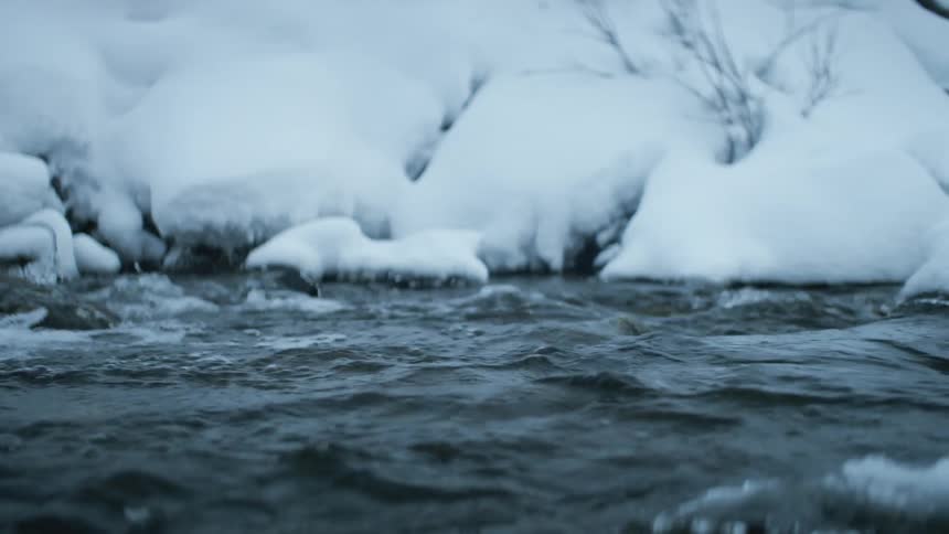 A river with water and rocks with snow and ice in the background
