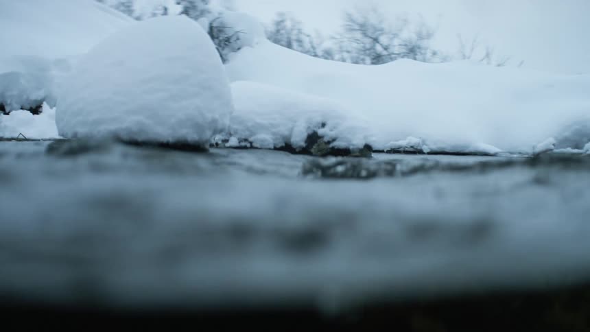 Stream water flows along a fixed route by snowy bank