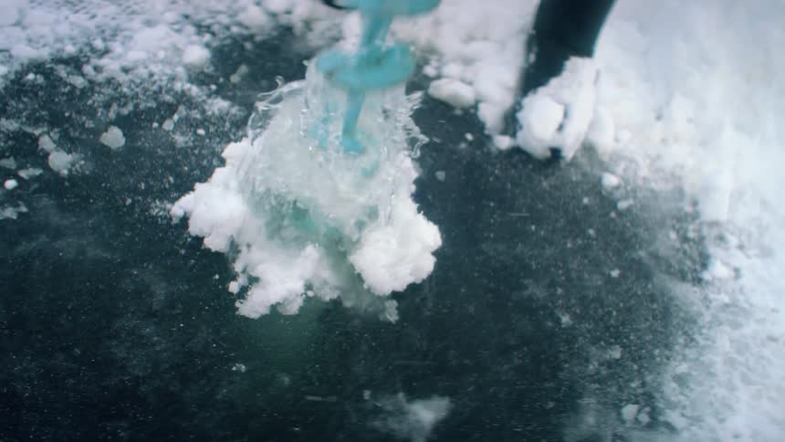 A person using a drill to drill a hole in ice water and snow