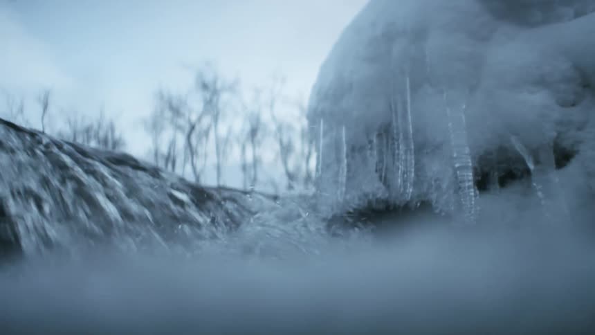 Water rushing from a small waterfall down a river surrounded by ice and frost in a forest during the day