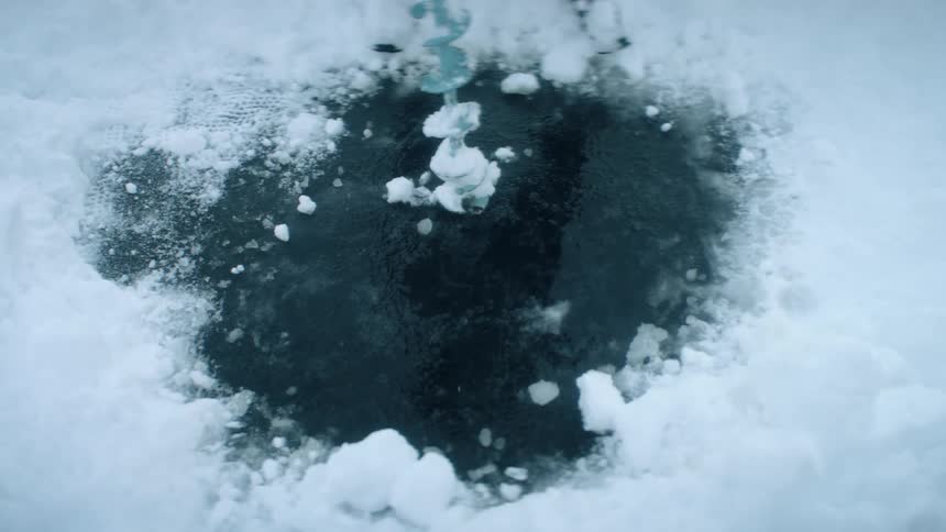 A person uses a drill to open a hole on the surface of a frozen lake